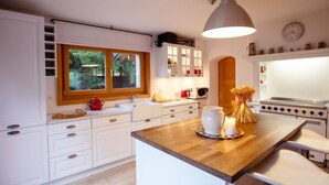 A modern kitchen with white cabinetry, a wooden island, a large pendant light, and a view of the outdoors through a window. - Chalet Le Haut Pré by Interhome (Villars)