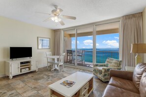 A spacious living room with a flat-screen TV, a ceiling fan, a balcony with a view of the ocean, and a leather sofa. - GULF FRONT! Majestic Tower One, 15th Floor (Panama City Beach)
