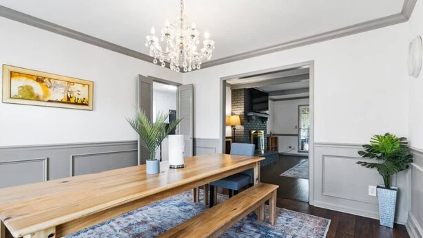 A dining area with a wooden table, benches, a chandelier, and a patterned rug.