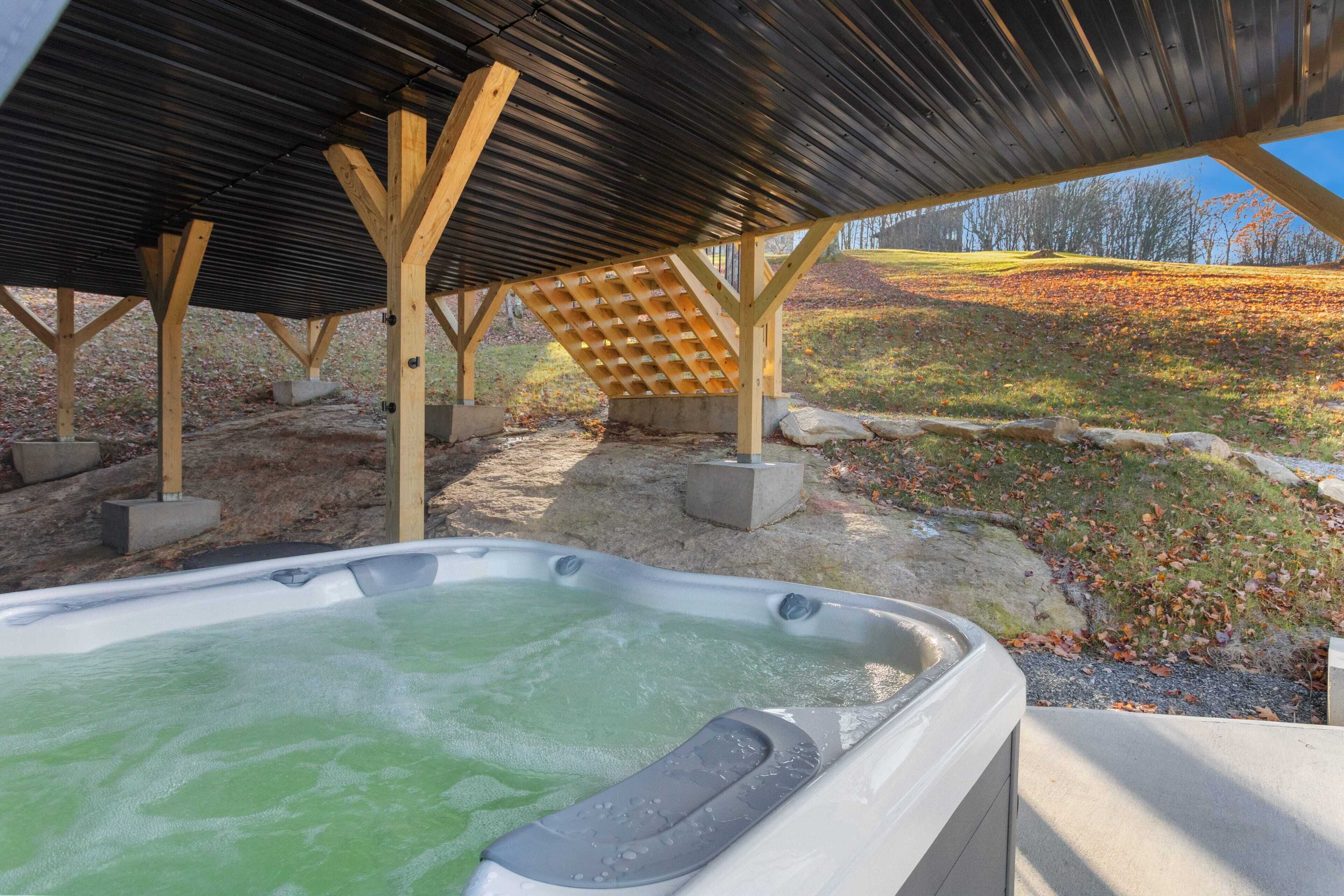 Un bain à remous installé sous une pergola en bois, avec vue sur une colline verdoyante.