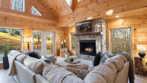 A cozy log cabin interior with a stone fireplace, large windows, and a comfortable seating area. - Beech Mountain Cabin on Golf Course (Beech Mountain)