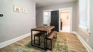 Uma área de refeições com mesa e banco de madeira, tapete estampado e obras de arte emolduradas na parede.