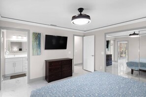 A bedroom with a bed, dresser, TV, and a ceiling fan. - Villa Albatross- Gorgeous Ground Level Pool Home in the Dunes (Sanibel)