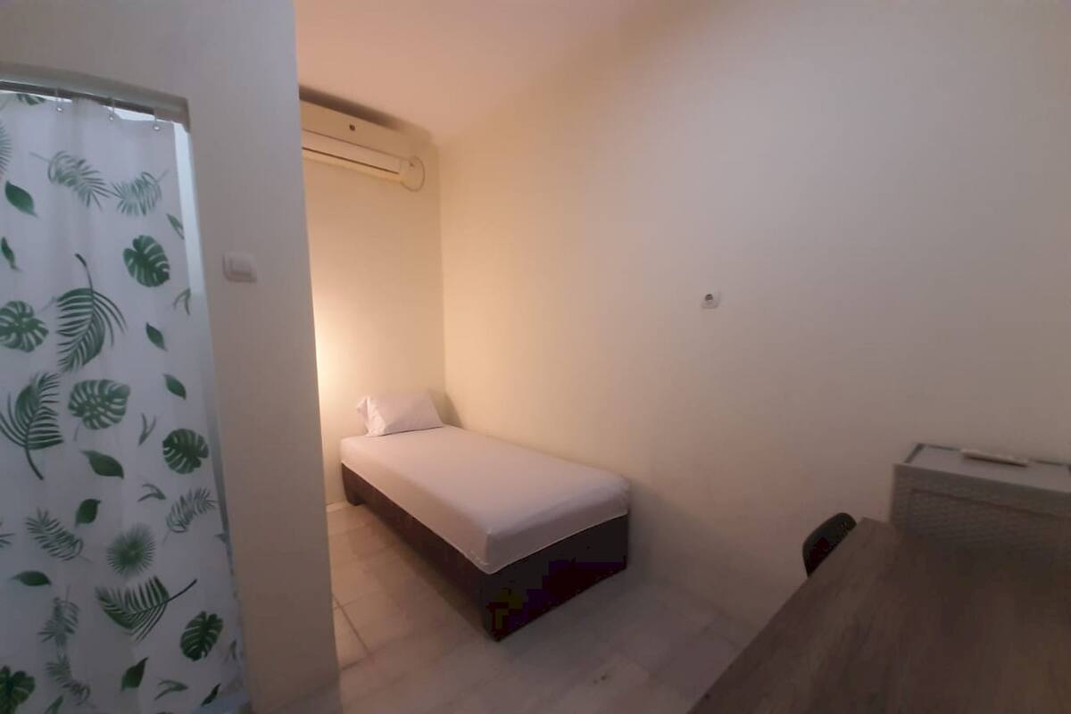 Ein kleines Zimmer mit einem Einzelbett, einem Holztisch und einem Vorhang mit Blätermotiv.