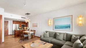 Una sala de estar moderna con un sofá, una mesa de comedor con sillas, una zona de cocina con refrigerador y microondas, y un cuadro grande en la pared.