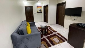 A living room with a grey sofa, a coffee table, a patterned rug, and a TV mounted on the wall. - Rawat Al Msaif (Taif)