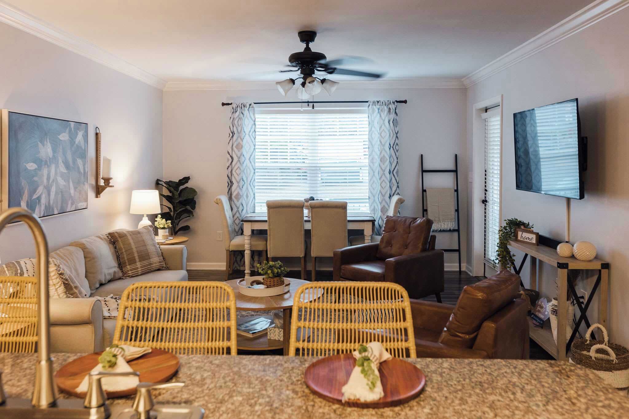 A living room with a dining area, a ceiling fan, a TV, and a window with curtains.