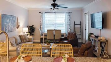 A living room with a dining area, a ceiling fan, a TV, and a window with curtains.