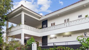 Ein zweistöckiges Gebäude mit einem Balkon im oberen Geschoss, einem überdachten Bereich im Erdgeschoss und einer schwarzen Wand mit Fenstern im oberen Geschoss.