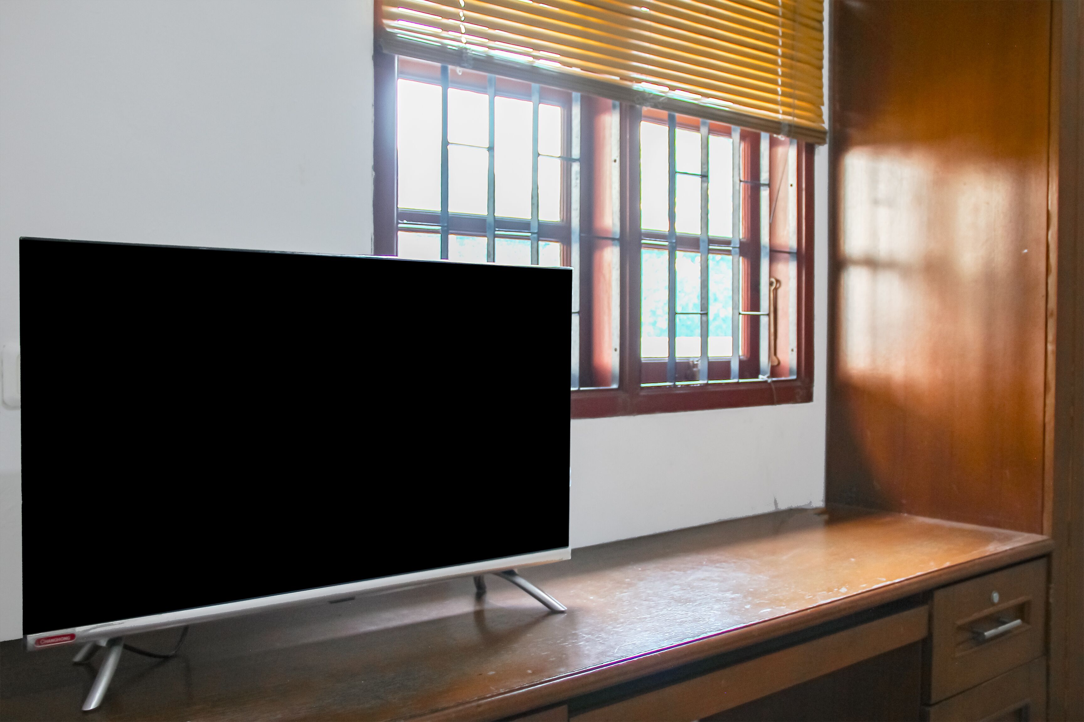 Een flatscreen-tv op een houten bureau, met een raam op de achtergrond.