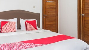 Ein ordentlich bezogenes Bett mit weißroter Bettdecke, zwei roten Kissen mit Muster und einem Holz-Kopfstück.
