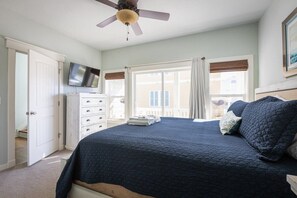 A bedroom with a bed, a ceiling fan, a TV, a dresser, and a window with curtains. - Tranquil Sunrises, Pool & Boardwalk Path to Beach! (Corolla)