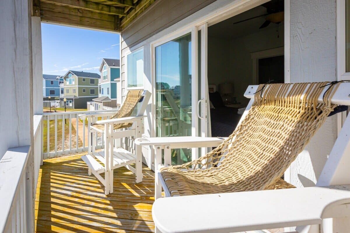 Um deck de madeira com cadeiras de lounge brancas e uma cadeira de vime, com vista para uma fileira de casas.