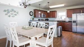 Una cucina moderna con mobili in legno, elettrodomestici in acciaio inossidabile e un'area pranzo con sedie bianche e un tavolo in legno.