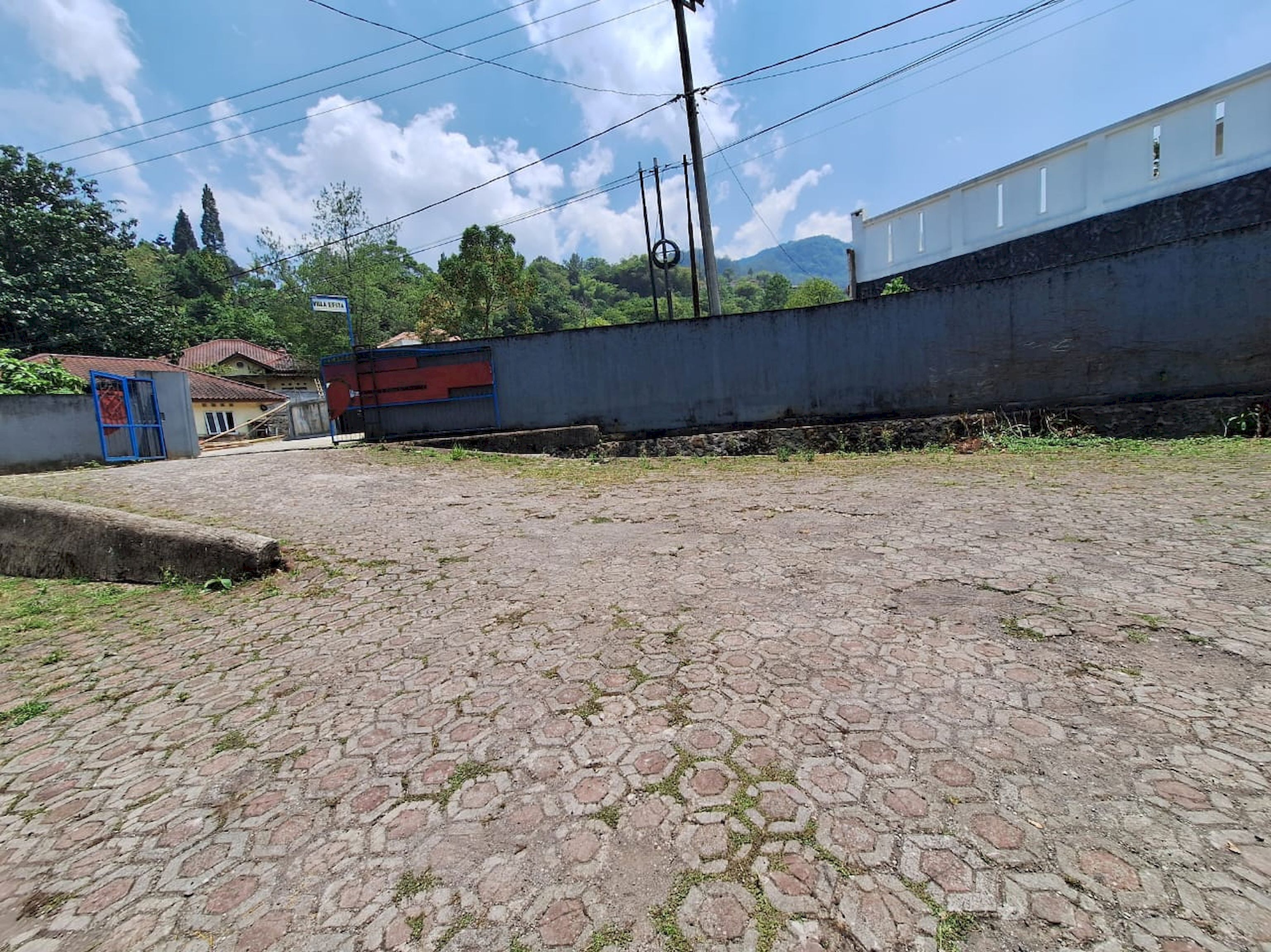 A paved area with a red gate, a blue building, and a white building in the background.