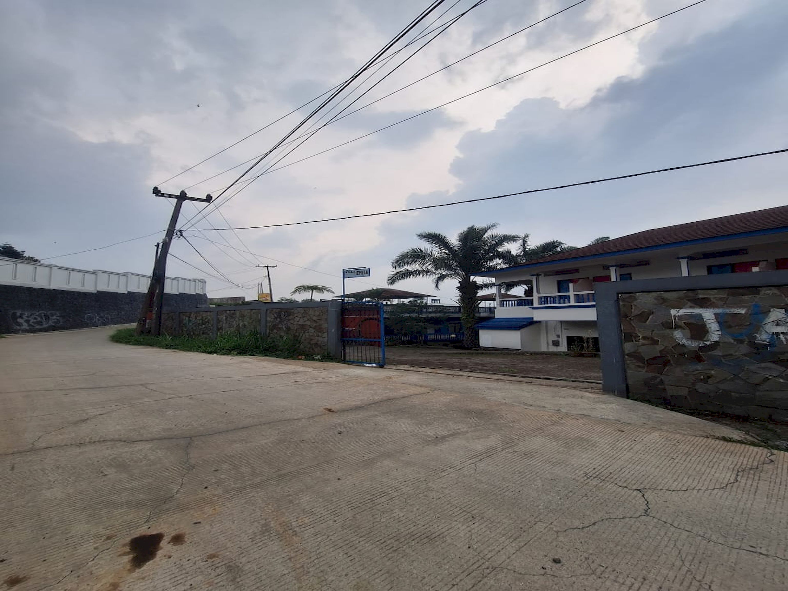 Un edificio con entrada porticada, muro de piedra y una palmera.