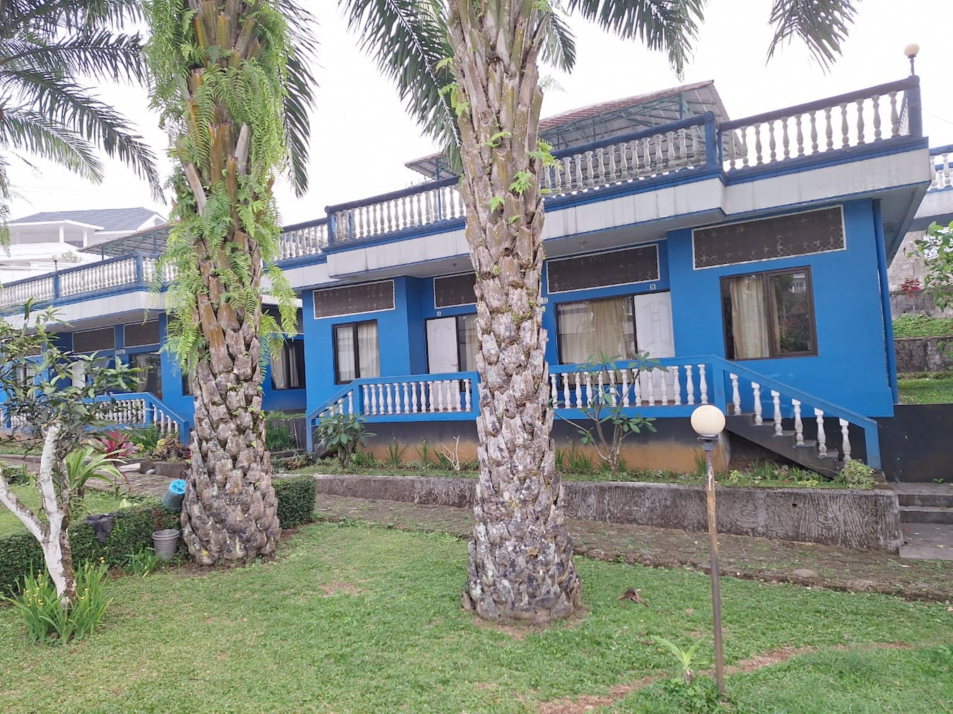 A blue building with balconies, surrounded by palm trees and a well-maintained lawn.