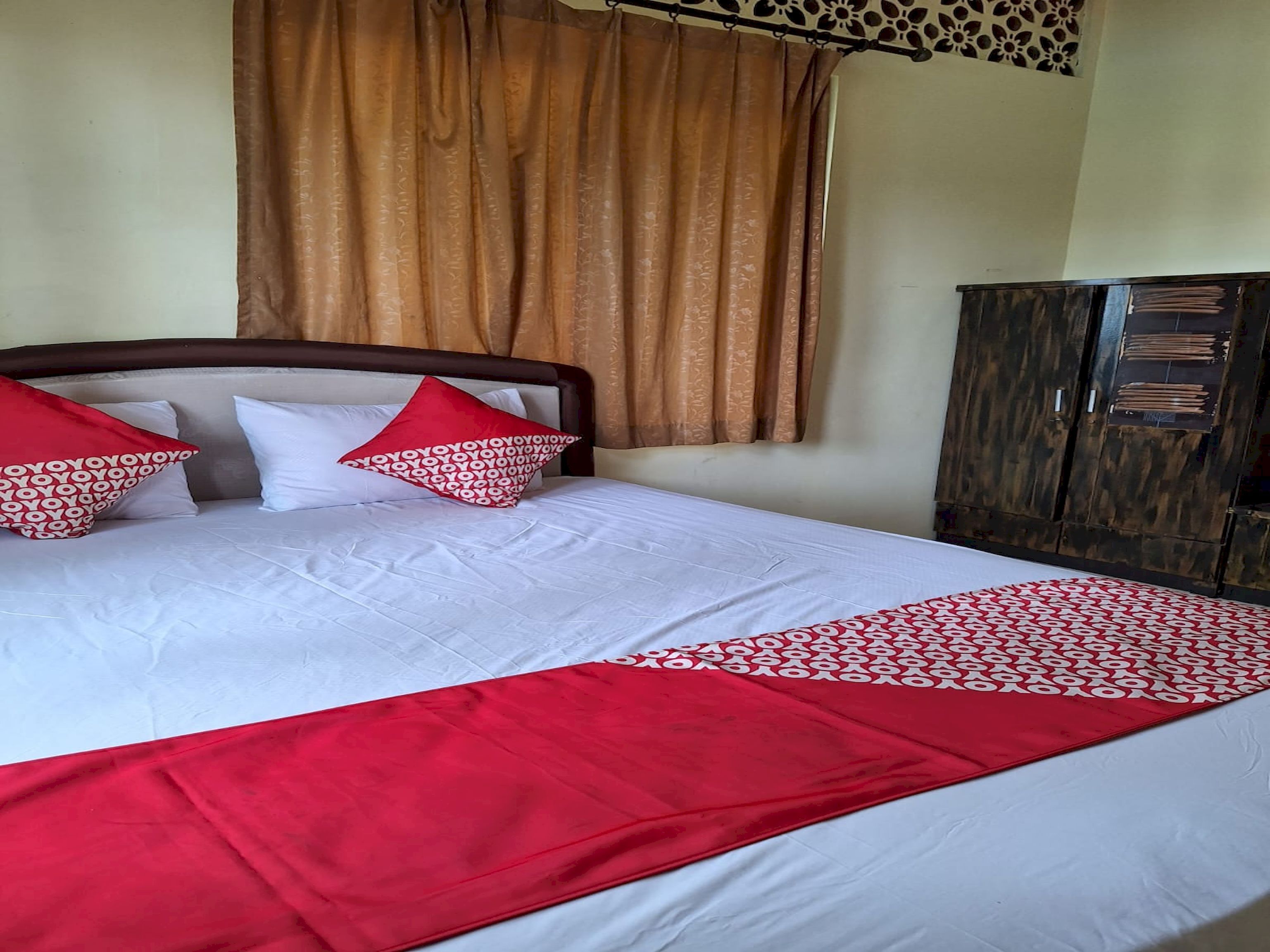 A neatly made bed with white and red bedding, a wooden headboard, and a brown curtain.