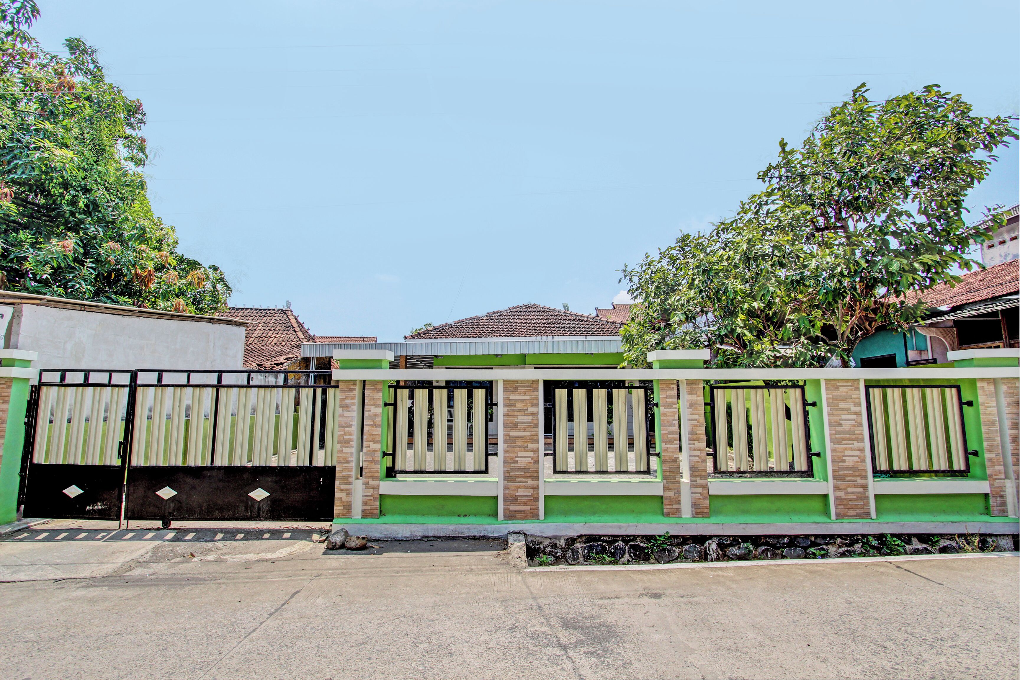 A gated residential area with a paved entrance and a green and beige wall.