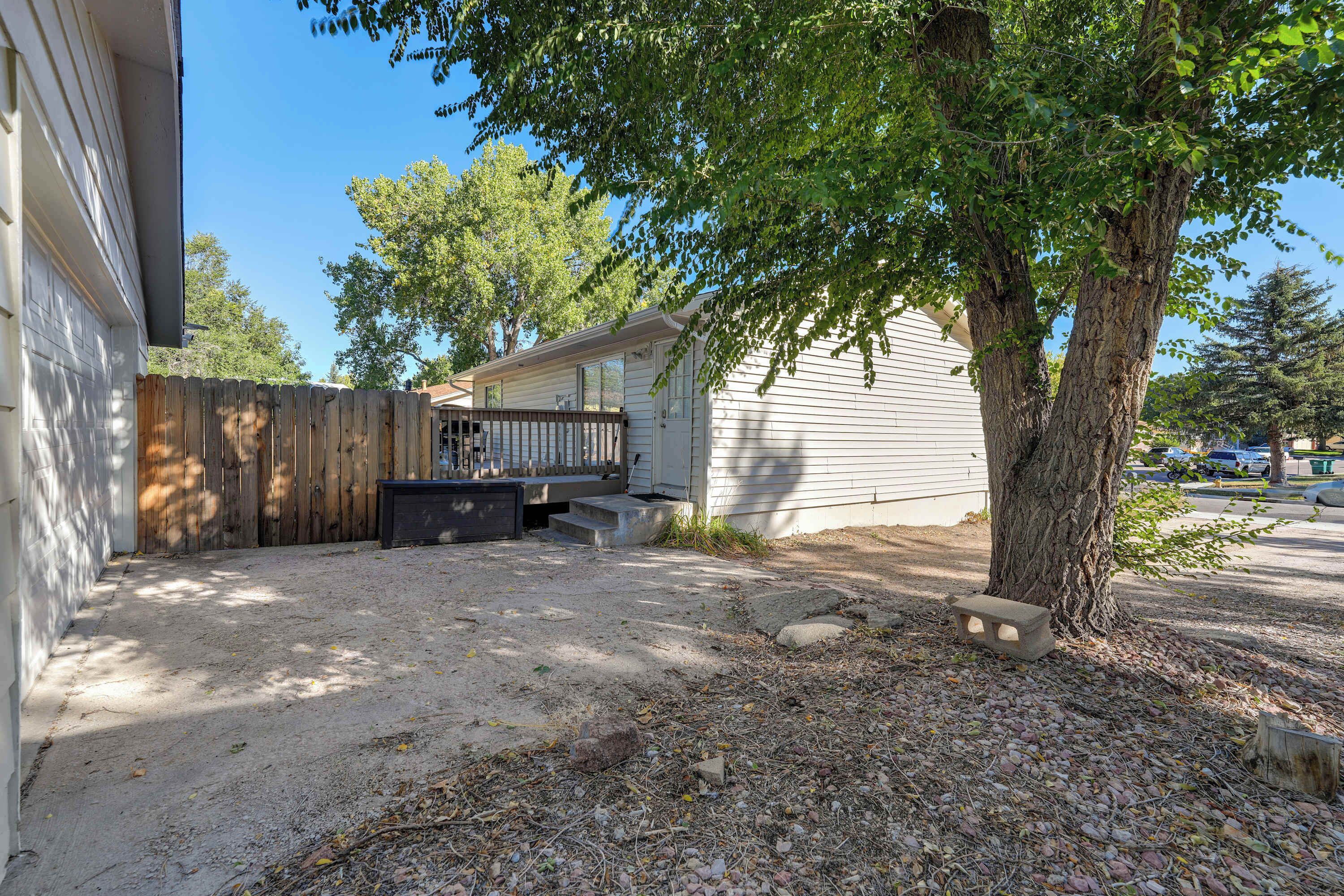 A residential property with a fenced backyard, a wooden deck, and a large tree providing shade.