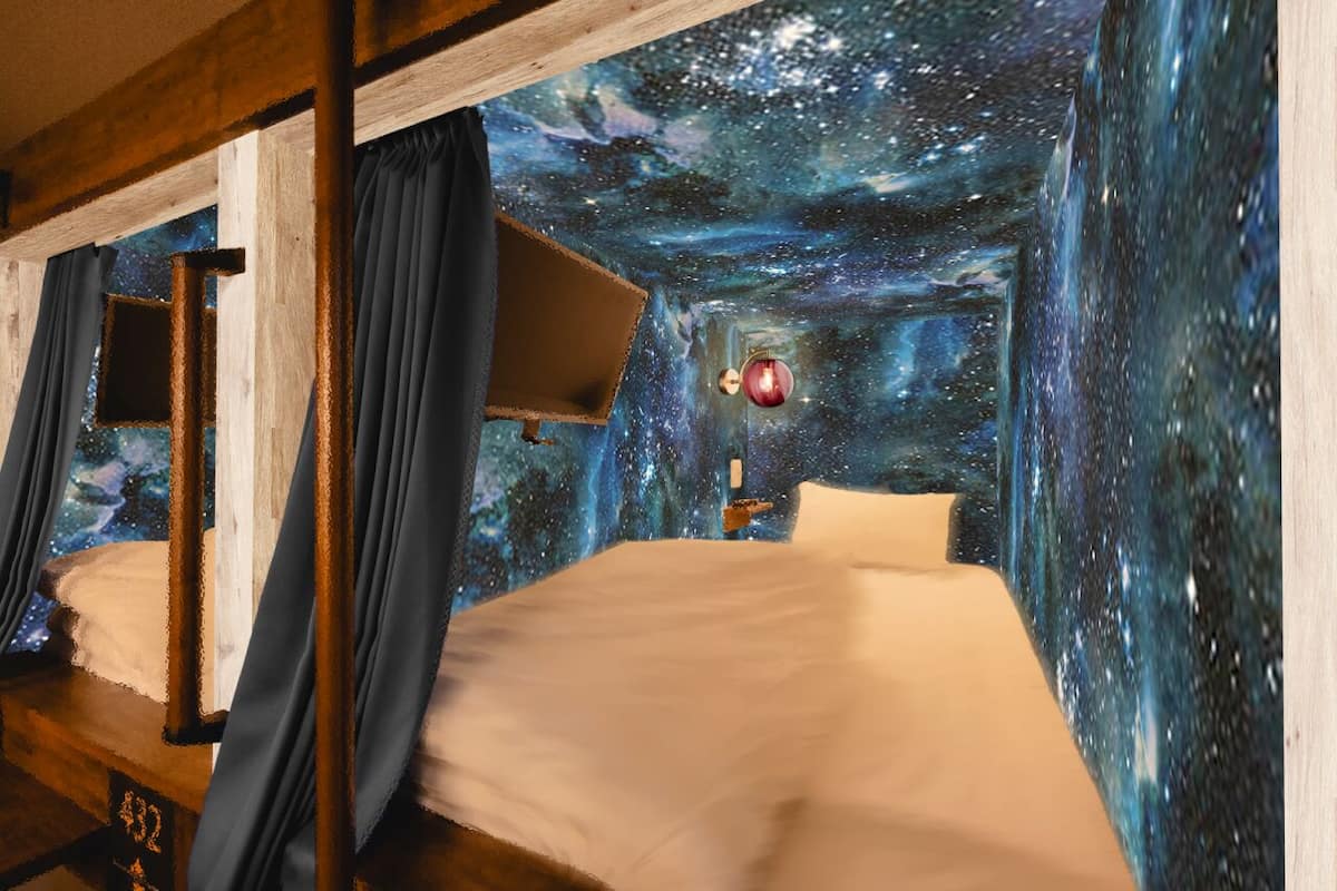 A room with a bed, a nightstand, and a wall mural depicting a starry night sky.