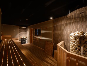 A modern interior with a wooden bench, a wall-mounted heater, and a stack of logs. - The Centurion Sauna Rest & Stay Sapporo Male Only (Sapporo)