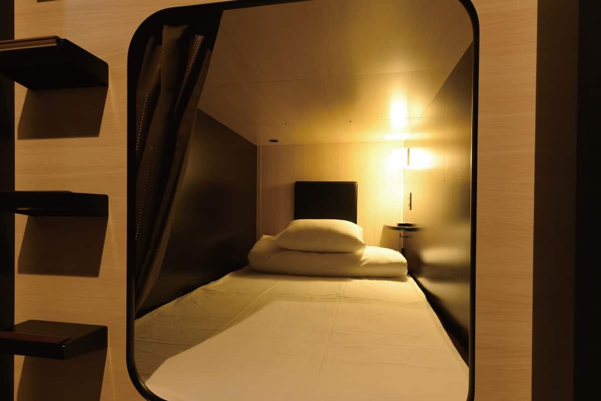 A compact room with a bed, a bedside table, and a wall-mounted light fixture.