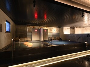 A modern indoor pool with a glass barrier, wooden deck, and a ceiling with red lights. - The Centurion Sauna Rest & Stay Sapporo Male Only (Sapporo)