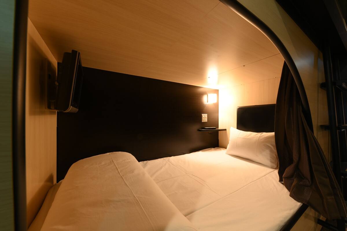 A compact, modern bedroom with a curved ceiling, a single bed, a mounted TV, and a bedside table with a lamp.
