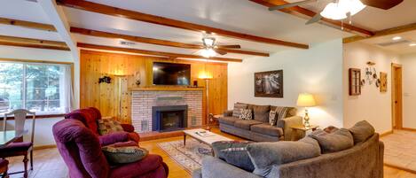 A spacious living room with a fireplace, wooden beams, a ceiling fan, and a dining area with a table and chairs.