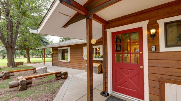 Eine Holzhütte mit roter Tür, einer Veranda und einer kleinen Sitzgelegenheit im Freien.