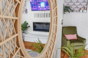 A cozy living room with a white brick fireplace, a green sofa, and a television mounted above it.