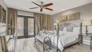 Ein Schlafzimmer mit Bett, Nachttischlampen, Deckenventilator, Glastisch und Vorhängen.