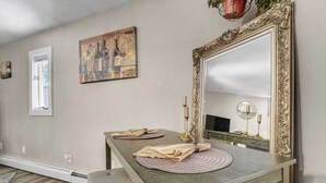 Ein Essbereich mit einem für zwei Personen gedeckten Tisch, einem großen, verzierten Spiegel und einem Weinflaschen-Gemälde an der Wand.