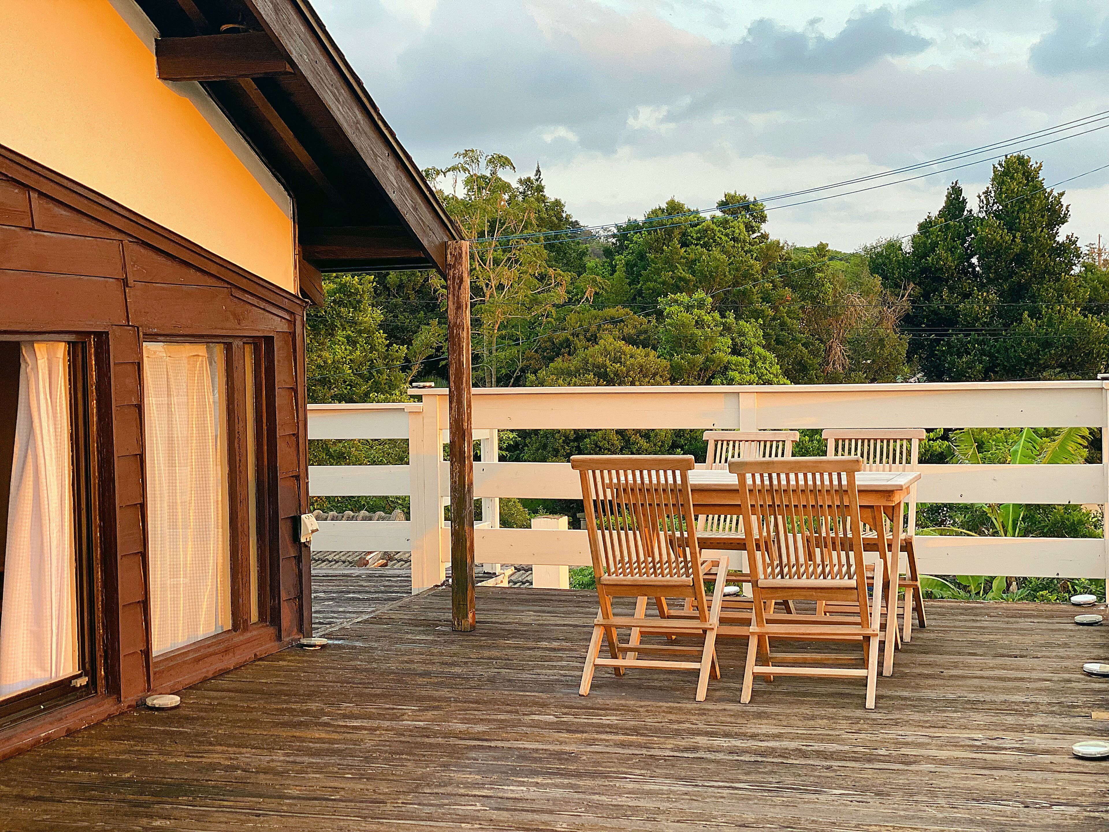 A wooden deck with a table and chairs, a white fence, and a building with a brown roof and windows.