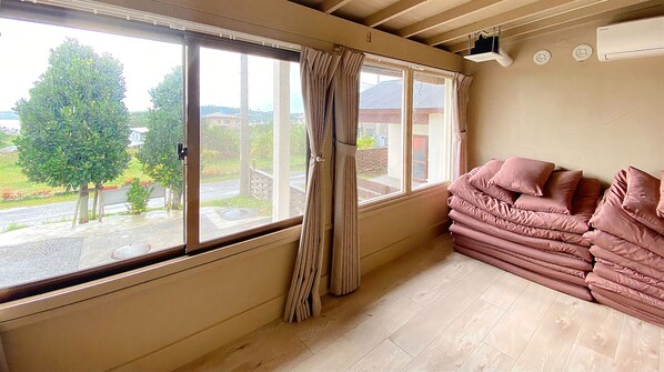 Una habitación con un ventanal grande, una cortina color beige y una pila de almohadas rosas.