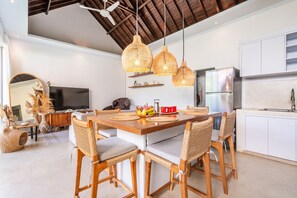 A modern kitchen with a dining area, featuring a large island, wicker chairs, and pendant lighting. - 3-Bedroom Jungle Amaranth Villa with Private Pool (Kabupaten Badung)