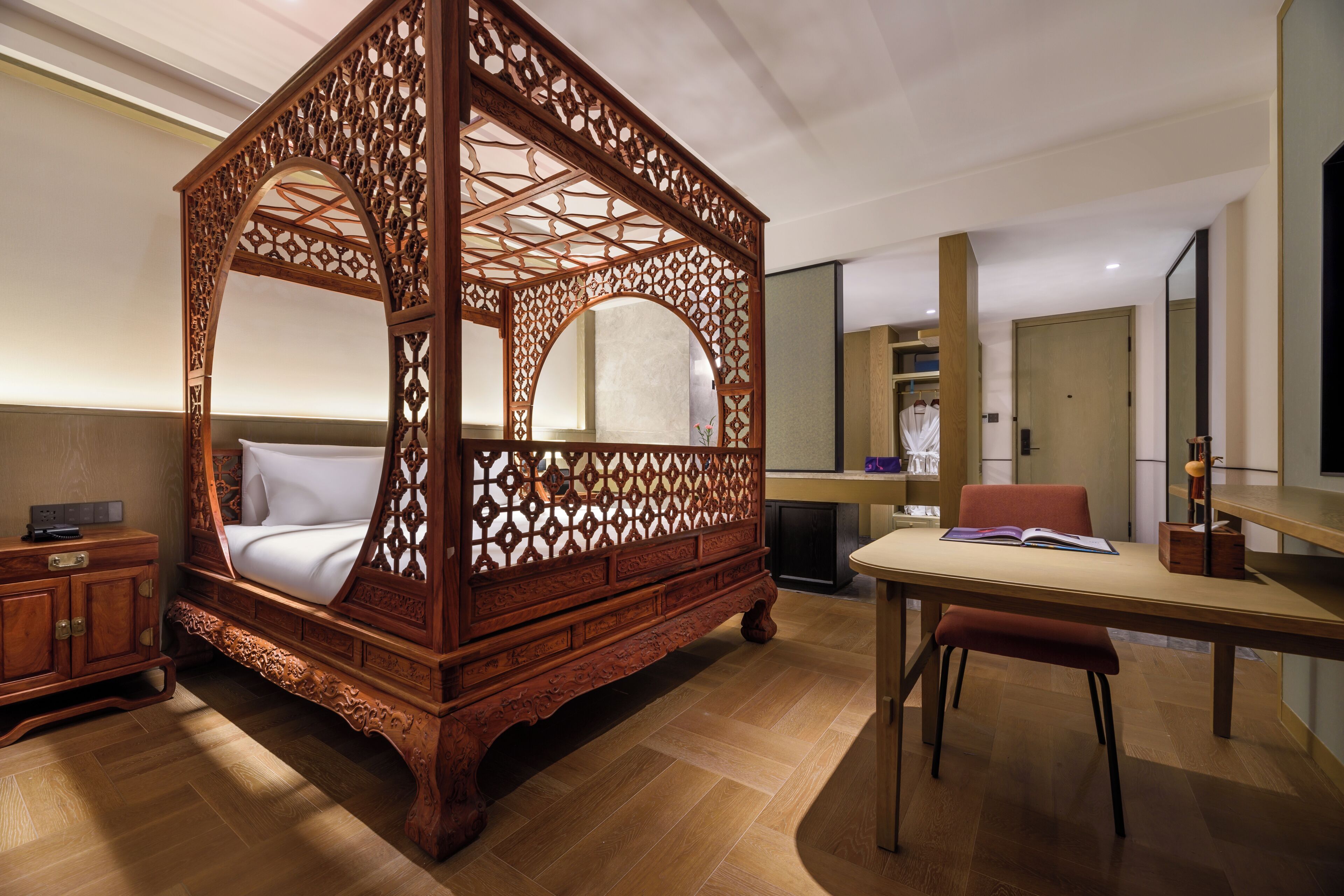 A four-poster bed with intricate woodwork, a wooden desk with a chair, and a mirror on the wall.