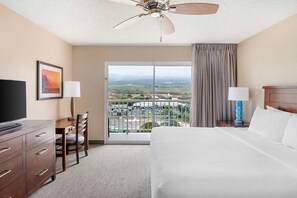 A hotel room with a bed, a desk, a television, a chair, a balcony with a view, and a ceiling fan. - Maui | Scenic Island Stay | Beach Access & Lagoon Pool (Maui)