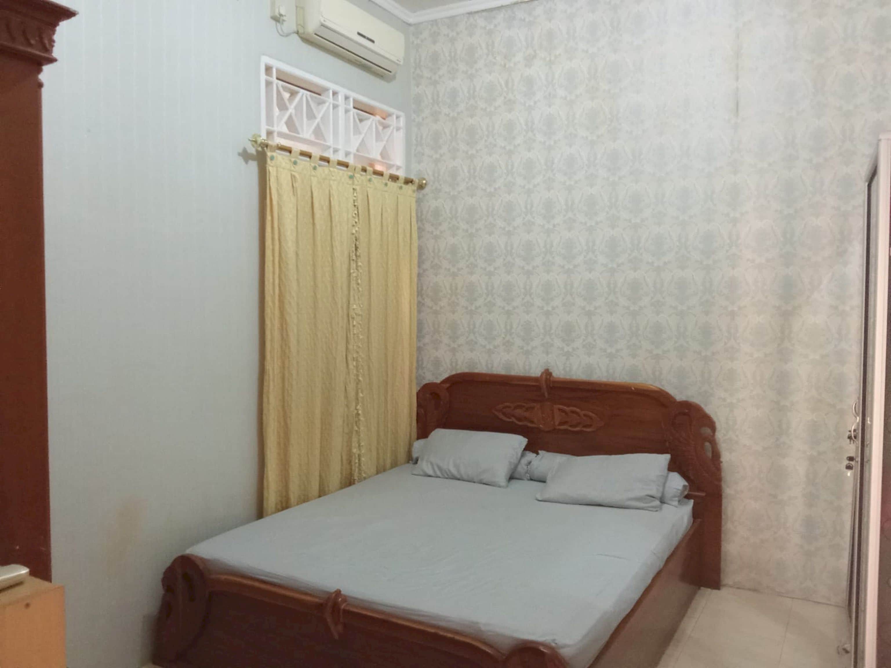 Una cama individual con cabecera de madera, pared lisa y papel tapiz estampado.