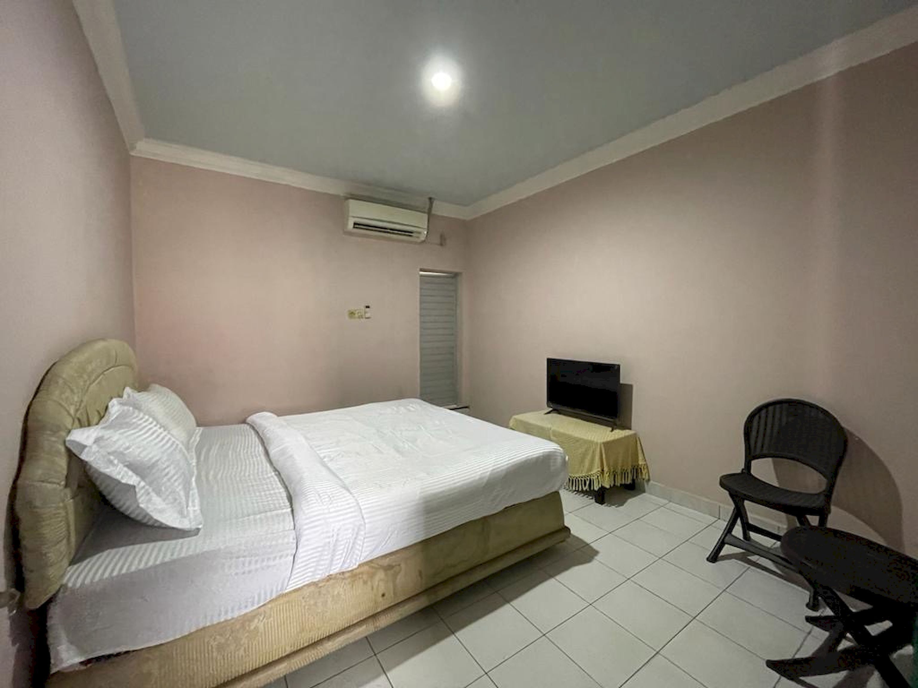 A bedroom with a bed, a television on a small table, a chair, and an air conditioning unit on the wall.
