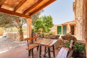 Relax in the serene patio area with benches and a table, surrounded by lush greenery and a traditional building.