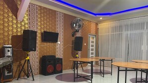 A room with a tiled floor, a piano, speakers, a TV, and a fan. - Hotel O Lima Saudara Syariah (Padang)
