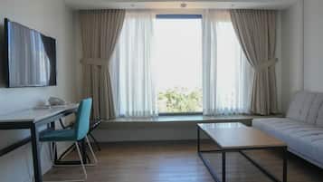 A modern hotel room with a desk, chair, sofa, and a large window with curtains.