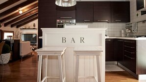 A kitchen with dark cabinets, a white countertop, and a bar area with two stools. - Entire Accommodation in Castelfranco Veneto (Castelfranco Veneto)