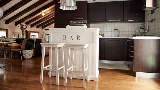 A modern kitchen with dark cabinets, a white bar area, and wooden flooring. - Entire Accommodation in Castelfranco Veneto (Castelfranco Veneto)