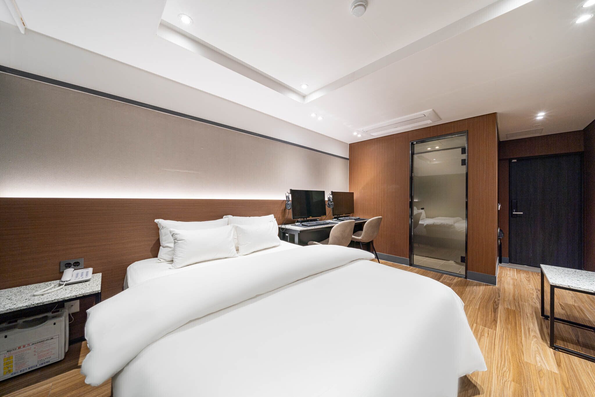 A modern hotel room with a large bed, a desk with a computer, a chair, and a wardrobe.