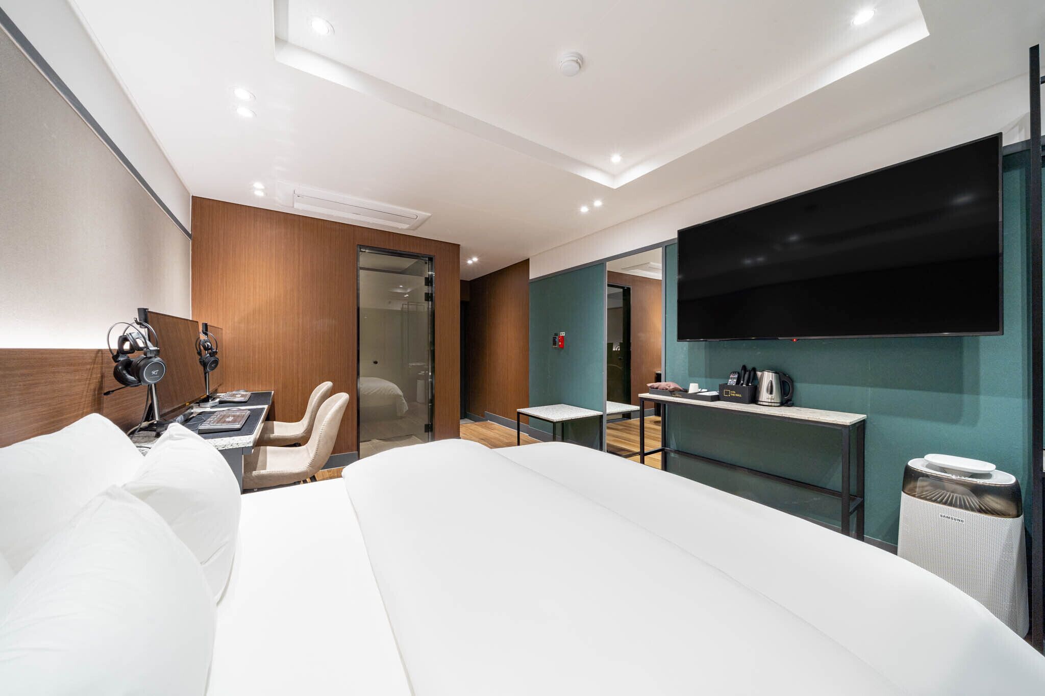 Una habitación de hotel moderna con una cama grande, un escritorio con silla, un televisor de pantalla plana en la pared y una mesita con hervidor.
