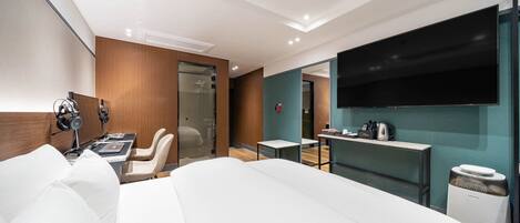 Una habitación de hotel moderna con una cama grande, un escritorio con silla, un televisor de pantalla plana en la pared y una mesita con hervidor.