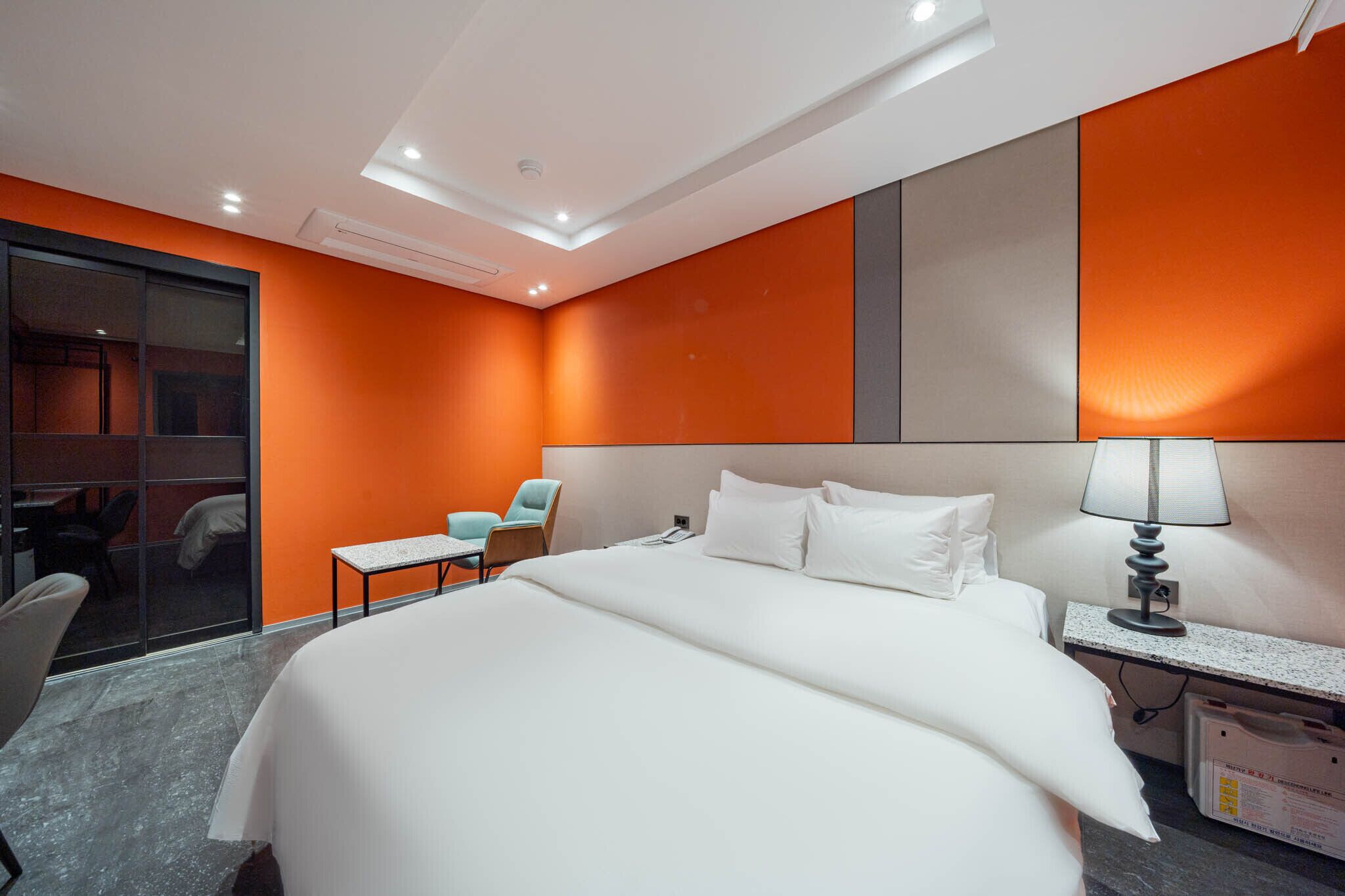 A hotel room with a large bed, a desk, a chair, and a glass partition.